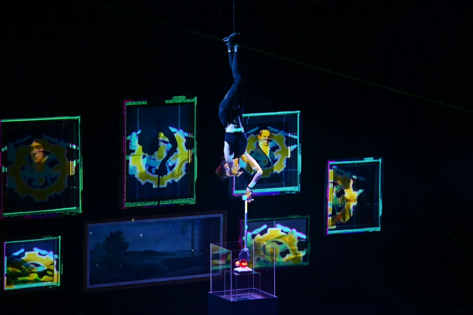Heist: an aerialist hangs head-down through the gallery, its frames filled with yellow patterns